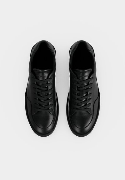 Ζευγάρι μαύρα δερμάτινα αθλητικά παπούτσια με κορδόνια, φαίνεται από πάνω σε λευκό φόντο.