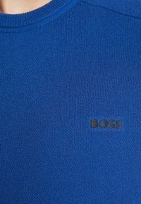 Maglione blu lavorato a maglia con scollatura rotonda e logo nero "BOSS" sul lato sinistro. Il tessuto presenta un aspetto tessuto e testurizzato.