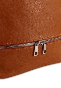 Close-up van een bruine leren tas met een gestructureerde textuur en twee zilveren ritsluitingen die elkaar ontmoeten in het midden van een horizontale rits.