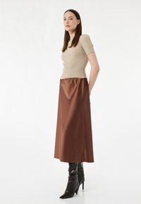Beige geribbelde top met korte mouwen, gecombineerd met een bruin satijnen rok tot de enkel en zwarte kniehoge puntige laarzen. Gladde texturen, getailleerd ontwerp.
