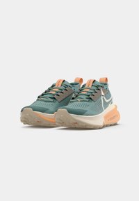 Blauw-groene sportschoenen met oranje accenten, een bovenlaag van mesh en een gestructureerde zool. Voorzien van grijze veters en een 'ZoomX' logo aan de zijkant.