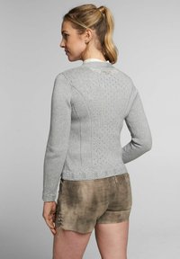Pull en tricot gris à manches longues, avec un motif texturé, un ourlet orné de dentelle décorative et des poignets côtelés. Associé à un short marron clair.