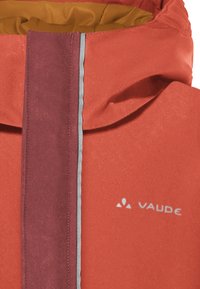 Rode waterdichte jas met een bordeauxrode ritsstrip, grijze accenten en een gele binnenvoering. Bevat een logo aan de onderzijde rechts.