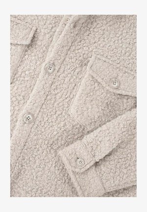 Hellgrauer, strukturierter Mantel aus fusseligem Stoff, mit zwei Brusttaschen und runden Knöpfen. Die Oberfläche zeigt ein weiches Boucle-Muster.