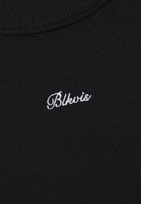 Tissu noir côtelé avec un col rond, arborant un texte brodé blanc qui indique "Blkvis" près du col.