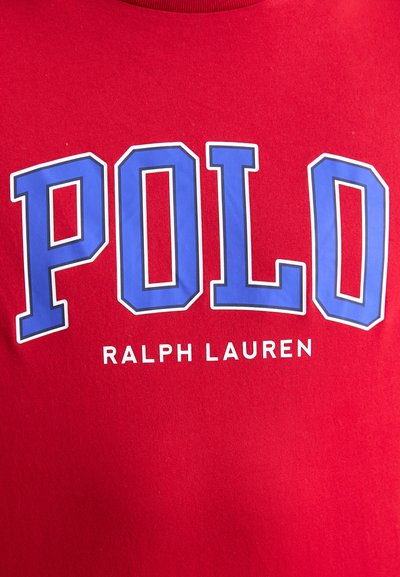 Piros pamut póló, nagy kék "POLO" felirattal és alatta kisebb "RALPH LAUREN" felirattal. Sima textúra, klasszikus szabás, kerek nyakkivágás.