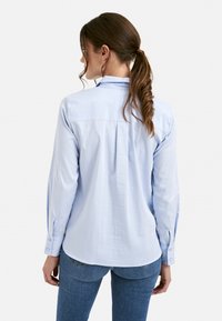 Light blue long-sleeve shirt in a smooth, lightweight fabric. Features a back yoke and buttoned cuffs, with a slightly curved hemline.