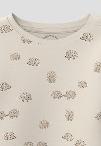 Jasny shirt z powtarzającym się wzorem jeża w stonowanych odcieniach. Miękka tekstura z okrągłym dekoltem i minimalistycznymi detalami projektu.