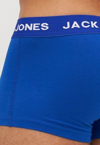 Blaue Baumwoll-Boxershorts mit einem breiten lila Bund, der "JONES JACK" in Weiß zeigt. Glatte Textur, enganliegendes Design mit sichtbarer Naht.