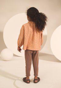 Blouse rose avec motif floral, manches bouffantes et col haut, associée à des leggings marron côtelés et des sandales foncées, vue de dos.