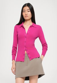 Fittet rosa cardigan med krage, lange ermer og frontlukking med knapper, kombinert med et beige miniskjørt. Strukturert stoff.