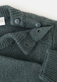 Tamno sivi pleteni materijal s dva plava dugmeta sašivena i odgovarajućim rupama za dugmad, prikazujući teksturu izbliza i detalje šivanja.