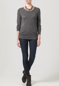 Grijze langiemouwen trui met een ronde halslijn, gecombineerd met donkerblauwe skinny jeans en enkellaarsjes. Opvallende zilveren statement ketting aanwezig.