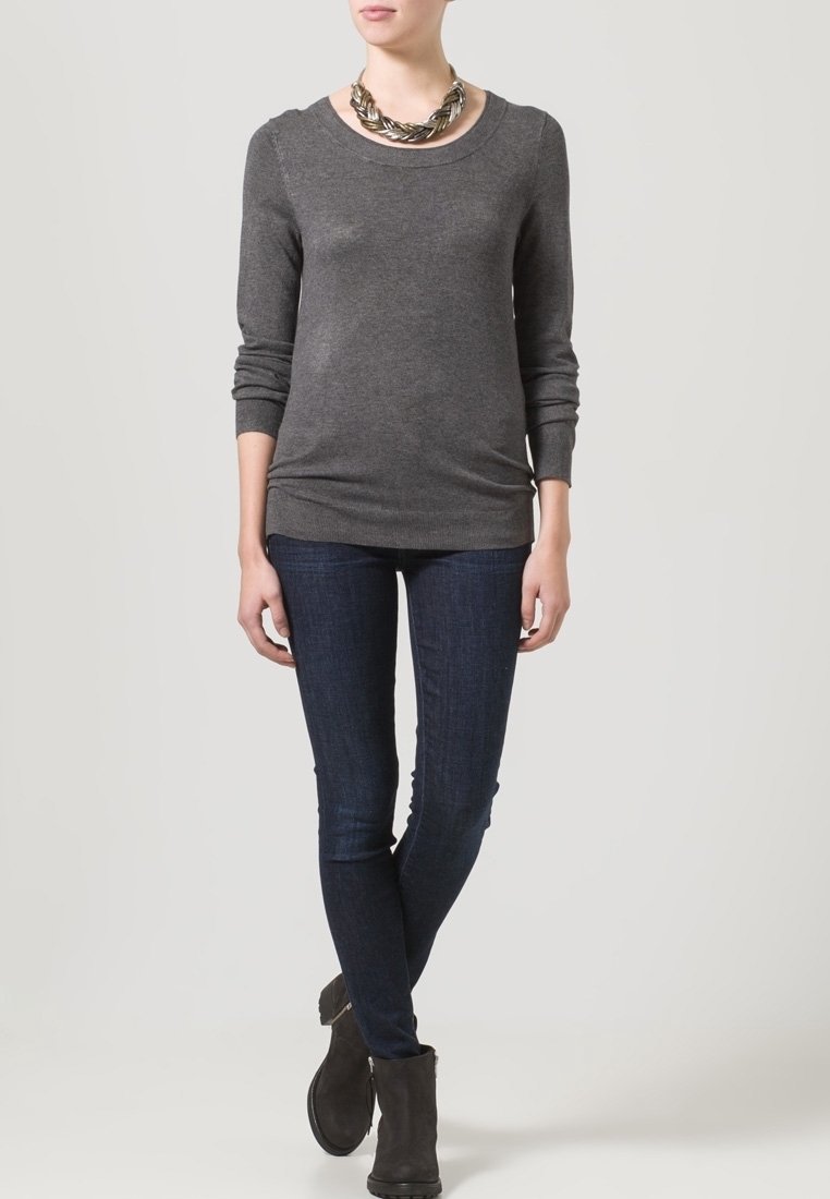 Grijze langiemouwen trui met een ronde halslijn, gecombineerd met donkerblauwe skinny jeans en enkellaarsjes. Opvallende zilveren statement ketting aanwezig.