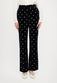 Námořnické sametové kalhoty s květinovým vzorem, které mají malé bílé a růžové květy, vysoký pas, rozšířené nohavice a hladkou texturu.