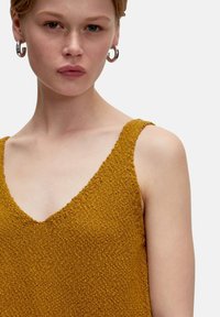 Senfgelbes, gestricktes Tanktop mit V-Ausschnitt und strukturiertem Material. Verfügt über breite Schulterträger und ein dezentes, weiches Finish.