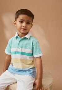 Helesinine polo särk valge kraega, millel on horisontaalsed triibud türkiissinises, valges, kollases ja sinises; sile tekstuur. Valged püksid.