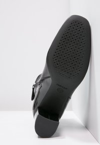 Czarne lakierowane botki za kostkę z niskim, prostokątnym obcasem i teksturowaną gumową podeszwą z perforowanym wzorem zapewniającym wentylację.