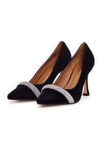 Scarpe nere in suede con tacco alto e punta affilata, caratterizzate da una fascia frontale adornata con strass luccicanti e tacchi geometrici sottili.