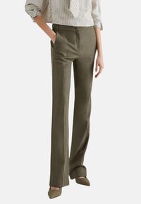 Pantaloni su misura verde oliva con tasche frontali, design a gamba dritta, tessuto texture e finitura liscia. Indossati con una blusa a righe.