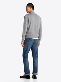 Hellgrauer Pullover mit hohem Kragen, kombiniert mit mittelblauen Jeans und schwarzen Slippern, von hinten betrachtet. Glatte Textur mit gerippten Bündchen.