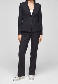 Navy blue tailored suit with a notched lapel blazer and matching trousers, featuring two front pockets and two buttons. Worn with white sneakers.