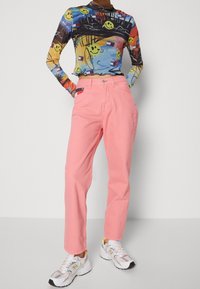 Top de manga larga y colorido con gráficos de caras sonrientes; pantalones rectos de color rosa claro; zapatillas blancas con acentos grises y amarillos.