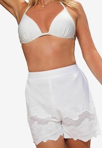 Fehér csíkos bikini felsőrész állítható pántokkal, fehér rövidnadrággal párosítva, amely csipkés díszítéssel és virágmintával rendelkezik az alján.
