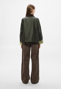 Roheline jakk pruunist kõrvetatud kaelusega ja kollaste aksentidega, kantud koos pruunide laia säärega pükstega, mis on sileda tekstuuriga.