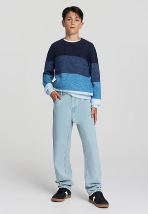 Maglione blu lavorato a maglia con strisce orizzontali in tonalità blu scuro e chiaro; abbinato a jeans in denim chiaro e sneaker nere.