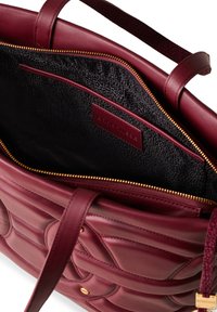 Borsa a mano in pelle borgogna con design trapuntato, zip dorata e interno testurizzato nero. Include tasca interna e etichetta con il marchio.