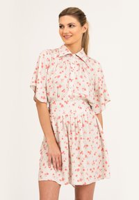 Kwiatowa sukienka z kołnierzykiem, krótkimi falbaniastymi rękawami oraz dopasowanym talią. Posiada jasnobeżowe tło z różowymi wzorami kwiatowymi.