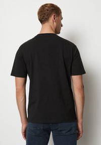Camiseta de algodón negra de manga corta con un corte relajado. Espalda sin costuras, cuello redondo y textura suave, combinada con jeans de color azul oscuro.