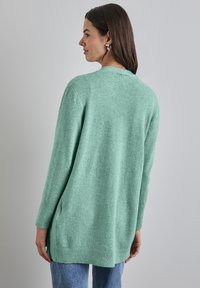 Hellgrüner, langer Cardigan aus weichem Strickmaterial. Mit gerippten Bündchen und Saum sowie einer lockeren Passform. Sichtbare Nähte.