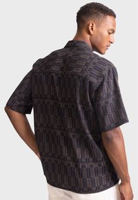 Camicia a maniche corte con bottoni di colore blu scuro, decorata con un motivo geometrico di piante, caratterizzata da una vestibilità rilassata e colletto a ribalta.