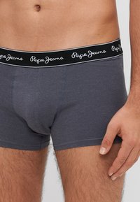 Sive pamučne bokserice s crnim pojasom na kojem se nalazi bijeli natpis "Pepe Jeans". Glatka tekstura i prilagođen dizajn s vidljivim šavovima.