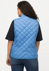 Gilet trapuntato azzurro chiaro con colletto alto, caratterizzato da motivi a rombi e una texture liscia, indossato sopra una camicia scura.