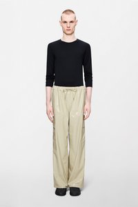 Μαύρο μακρυμάνικο τοπ σε συνδυασμό με μπεζ γυαλιστερό παντελόνι φαρδύ, με κορδόνι στη μέση και πλαϊνές τσέπες, συμπληρωμένο με μαύρα παπούτσια.