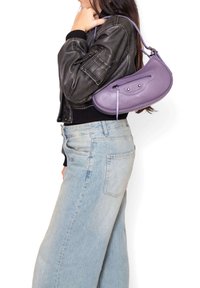 Borsa in pelle viola con forma curva e tasca con zip, indossata a spalla. Modello con giacca in pelle nera e jeans azzurri.