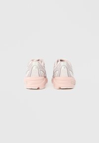 Világos rózsaszín és fehér futócipő pár hátulnézetből egy egyszerű szürke háttéren.