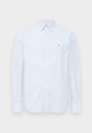 Chemise à manches longues bleu clair avec col boutonné et petit logo sur la poitrine gauche, présentée sur fond blanc.