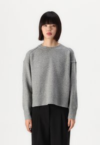 Grå strikkegenser med rund hals, senkede skuldre og ribbestrikket kant. Stoffet ser mykt ut med en litt fuzzy tekstur.