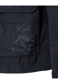 Granatowa kurtka z tkaniny z wyraźnym logo syrenki i wytłoczonym brandingiem "SCHOTT N" na kieszeni, z widocznym szczegółowym przeszyciem.