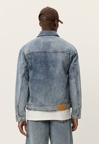 Τζιν μπουφάν σε ανοιχτό μπλε με κλασική κοπή, κουμπωτό μπροστά και τσέπη στο στήθος. Διαθέτει δερμάτινο λάστιχο κοντά στο τελείωμα με το όνομα της μάρκας.