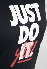 Svart t-shirt med stor vit text som lyder "JUST DO IT!" och en röd accent nedanför. Materialet verkar mjukt och tajt sittande.