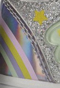 Primer plano de una zapatilla que presenta una estrella y un corazón plateados y brillantes, con rayas de arcoíris y pastel sobre una superficie reflectante.