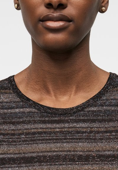 Κοντινό πλάνο ενός ατόμου που φοράει χρυσά σκουλαρίκια και ένα μαύρο, λαμπερό, ριγωτό τοπ με στρογγυλή λαιμόκοψη.