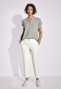 Top verde chiaro testurizzato con maniche corte, abbinato a pantaloni crema e sneakers beige. Il top presenta un delicato dettaglio sul collo.