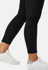 Białe sneakersy z szarymi akcentami i designem na sznurówki, zestawione z czarnymi jeansami typu skinny, mającymi dopasowany krój i lekki stretcze.