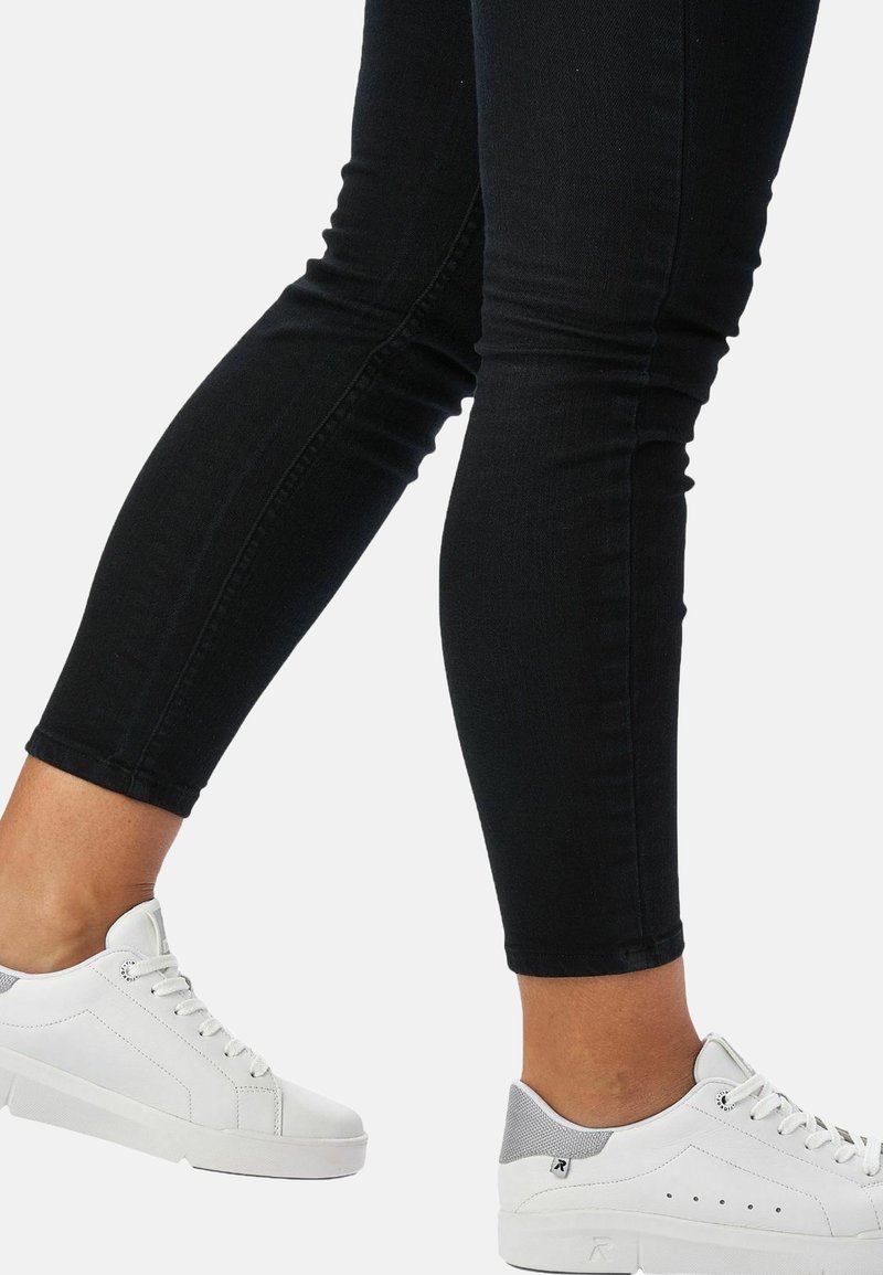 Białe sneakersy z szarymi akcentami i designem na sznurówki, zestawione z czarnymi jeansami typu skinny, mającymi dopasowany krój i lekki stretcze.